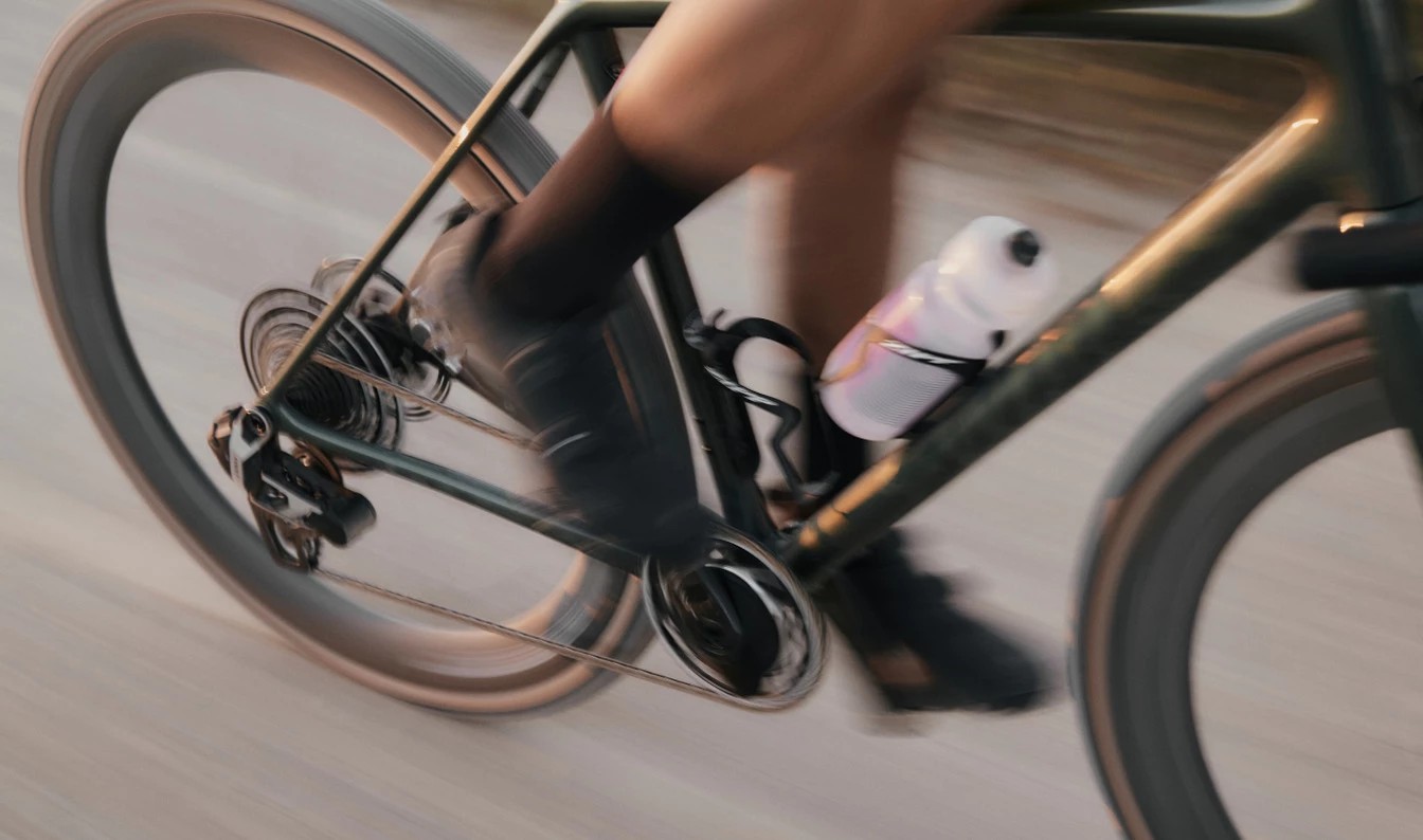 ロードバイクを高速で漕ぐサイクリストのクローズアップ。車輪や脚に動きのブレが見られる。.