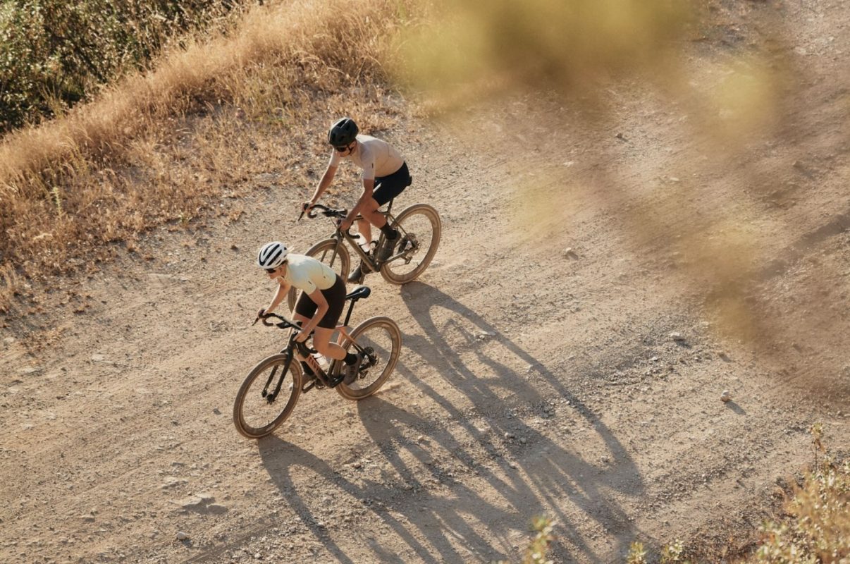 未舗装の道を、グラベルバイクに乗った2人のサイクリストが走っている。.