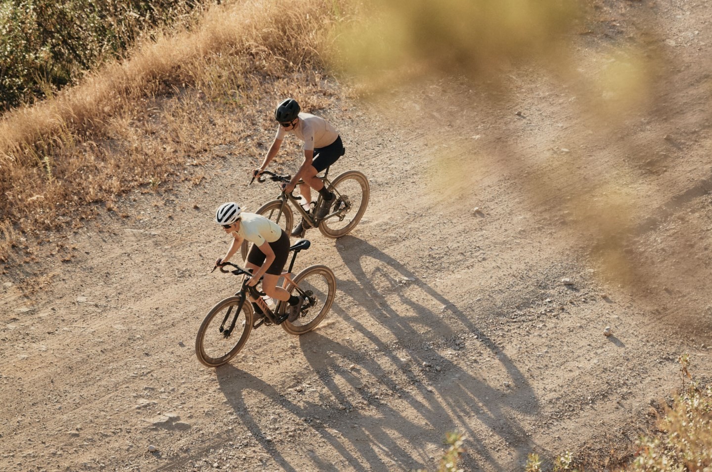 未舗装の道を、グラベルバイクに乗った2人のサイクリストが走っている。.