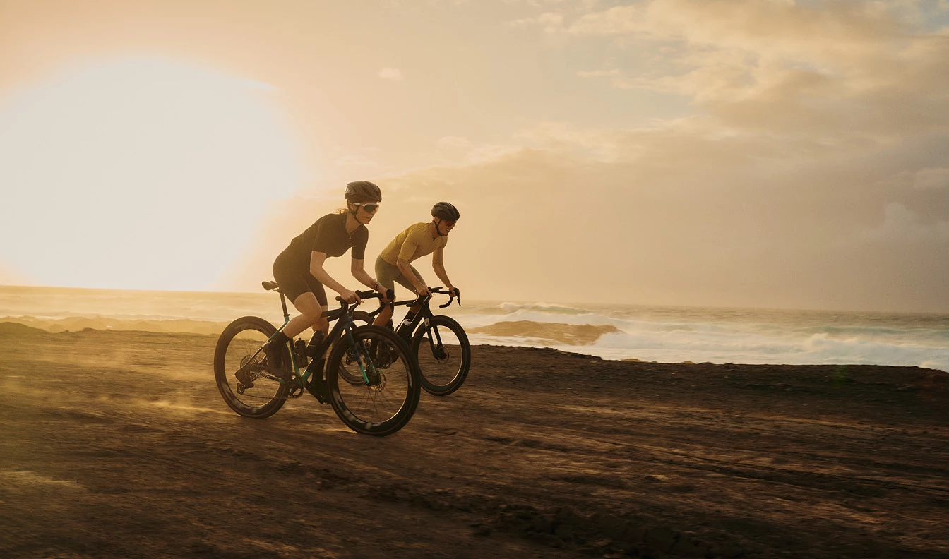 夕暮れ時、海沿いの未舗装の道を走る2人のサイクリスト。.