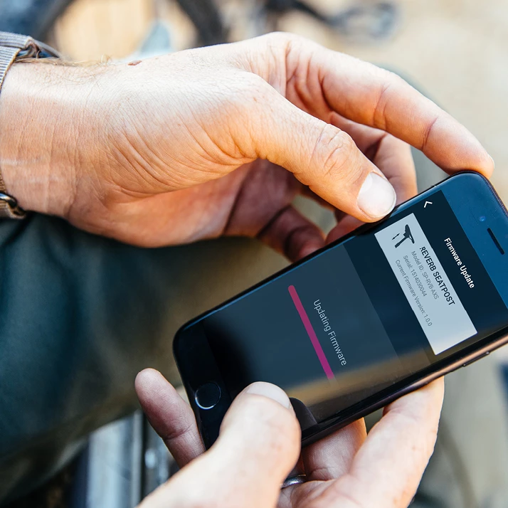 Reverbシートポストのファームウェア更新画面が表示されたスマートフォンを手に持つ手。.
