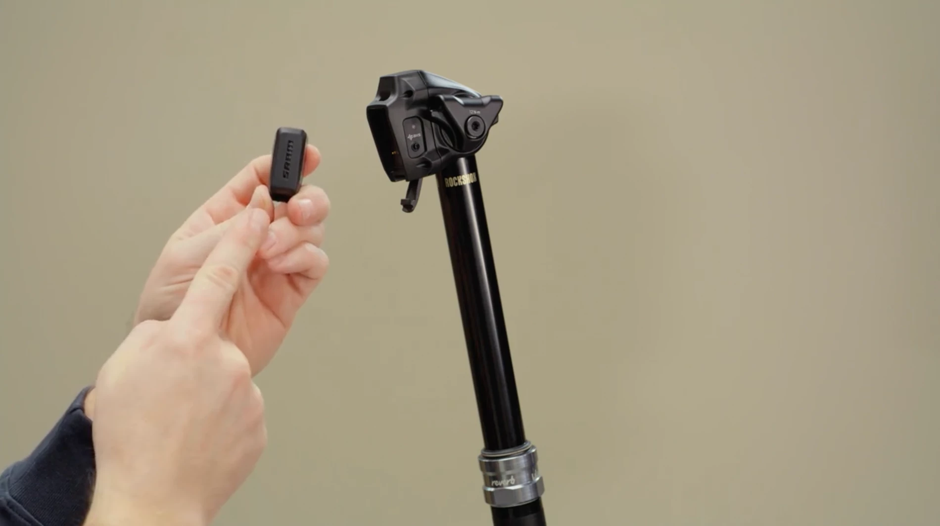 RockShox Reverbのドロッパーシートポストの横で、小さな黒いSRAMのバッテリーを手に持っている様子。.