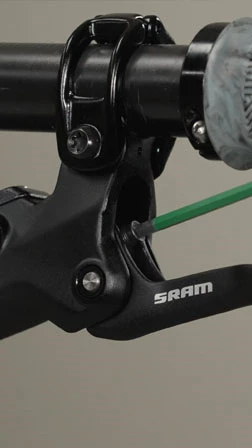 ハンドルバーに取り付けられたSRAM製の自転車ブレーキレバーを、六角レンチで調整している様子。.
