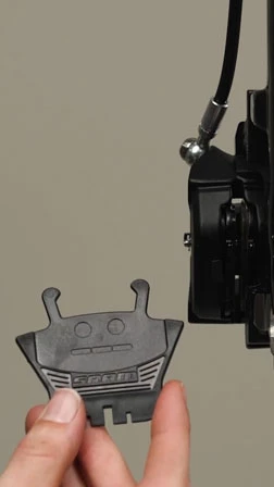 ブレーキキャリパーのそばで、SRAM製の自転車用ディスクブレーキパッドを手に持っている手。.