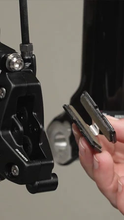 SRAM製のブレーキキャリパーの横で、自転車のディスクブレーキパッドを2枚手に持っている人物。.