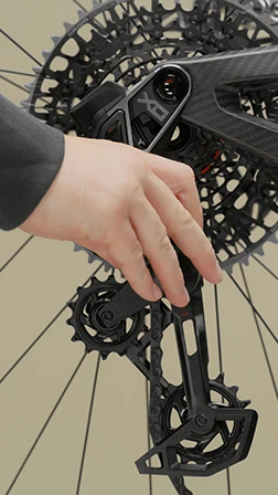 自転車のリアディレイラーとカセットに触れている手。.