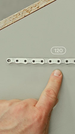 指が、120という番号が記された自転車のチェーンの一部を指し示している。.
