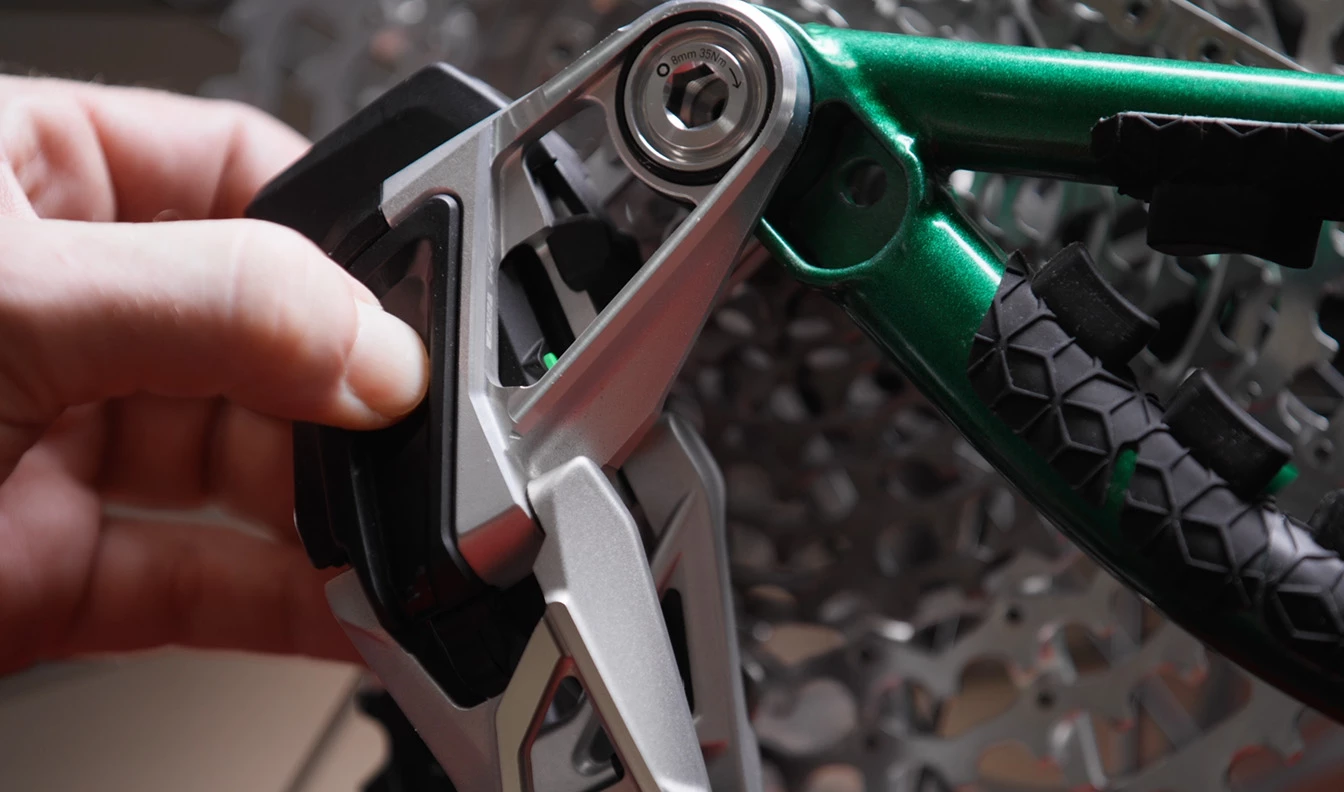緑色の自転車のフレームとディレイラーアセンブリのピボットポイントを調整している手。.