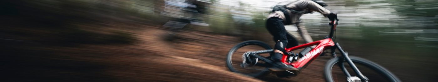 マウンテンバイクのライダーが、モーションブラーを伴いながら未舗装のトレイルを疾走している。.