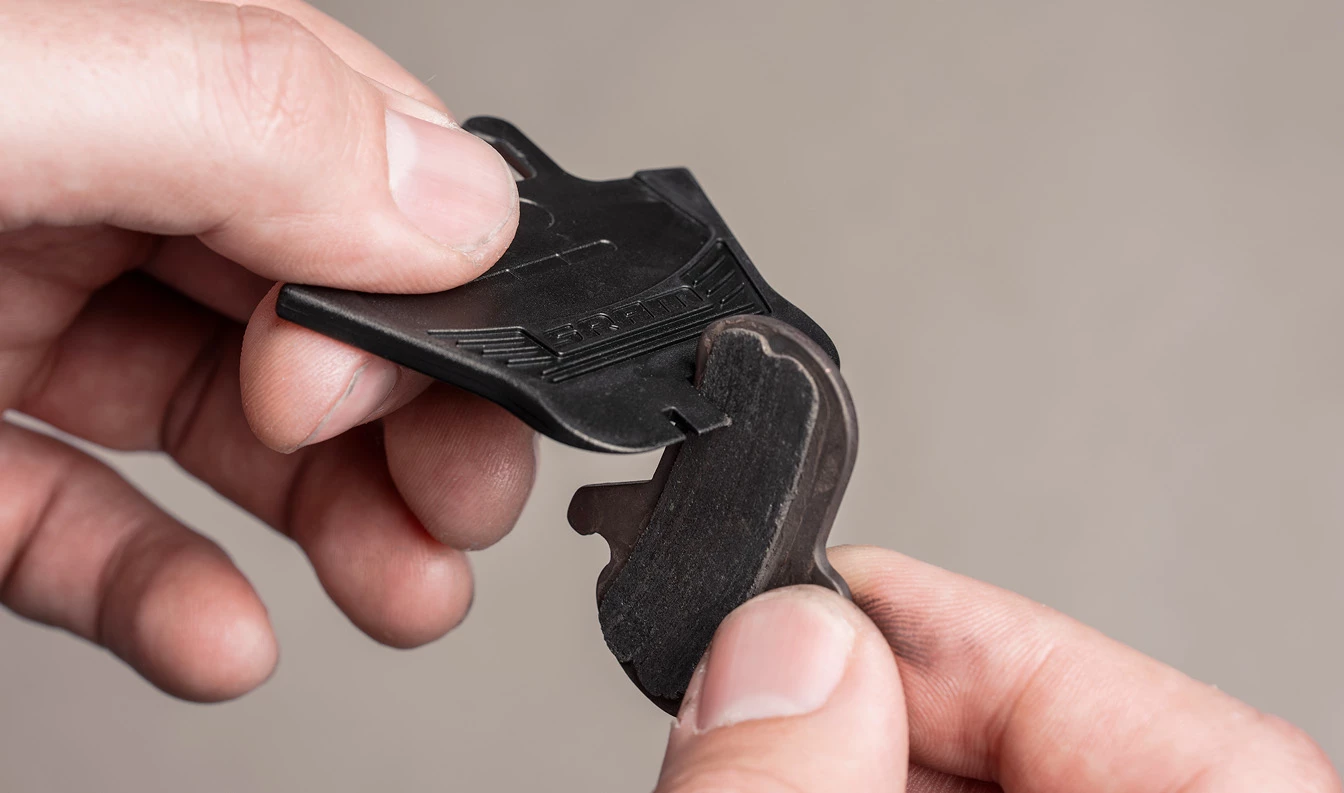 自転車のディスクブレーキパッドとその保護用のプラスチック製輸送カバーを手に持っている様子。.