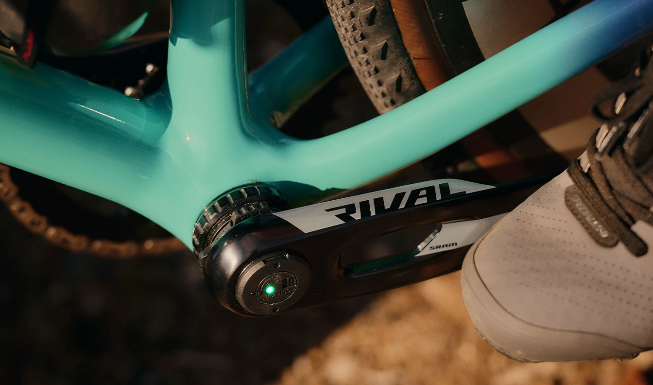ティール色の自転車フレームのクローズアップ。SRAM Rivalクランクセットが装着されており、パワーメーターには緑色のインジケーターライトが付いています。.