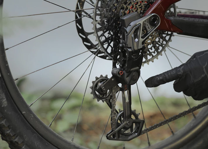 手袋をはめた指が、マウンテンバイクのディレイラーを指し示している。.