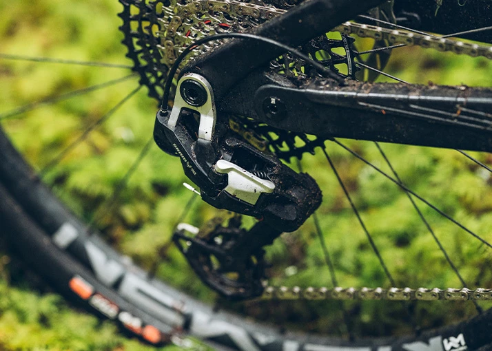 自転車フレームに取り付けられたSRAM製のマウンテンバイク用リアディレイラーとカセットのクローズアップ。部品には泥が飛び散っている。.