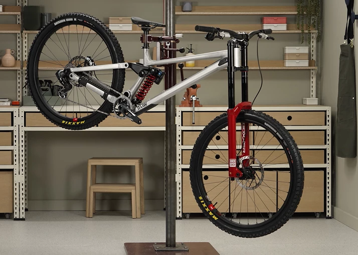 自転車修理スタンドに載せられた、シルバーのデュアルサスペンション付きマウンテンバイクで、フロントフォークは赤色である。.