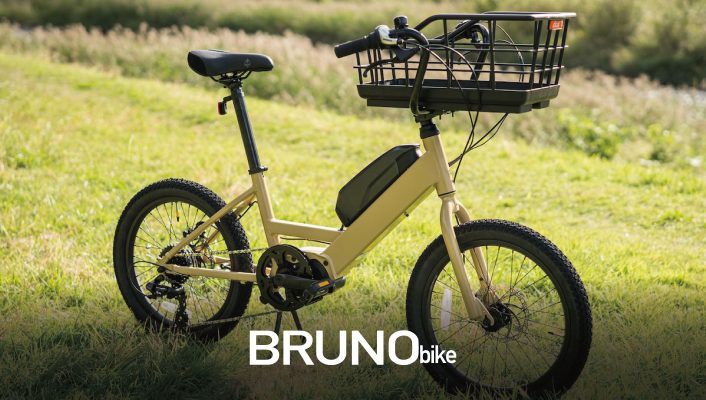 前部に収納バスケットが付いたベージュ色の電動自転車が、芝生の上に停められており、その下部にBRUNObikeという文字が重ねて表示されている。.