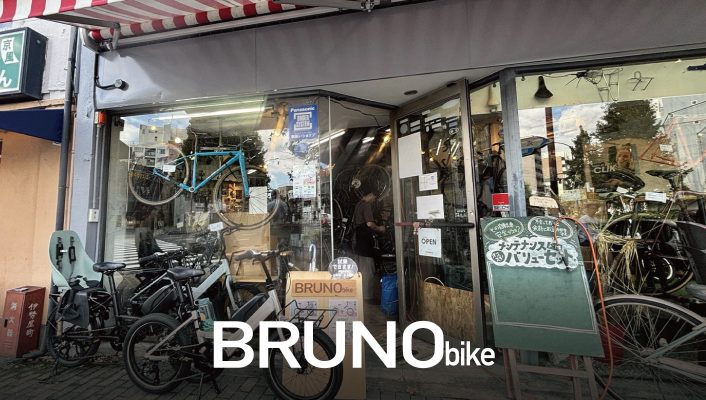 自転車店の外観。ショーウィンドウにはさまざまな自転車が並べられ、店の前には黒板の看板が掲げられている。.