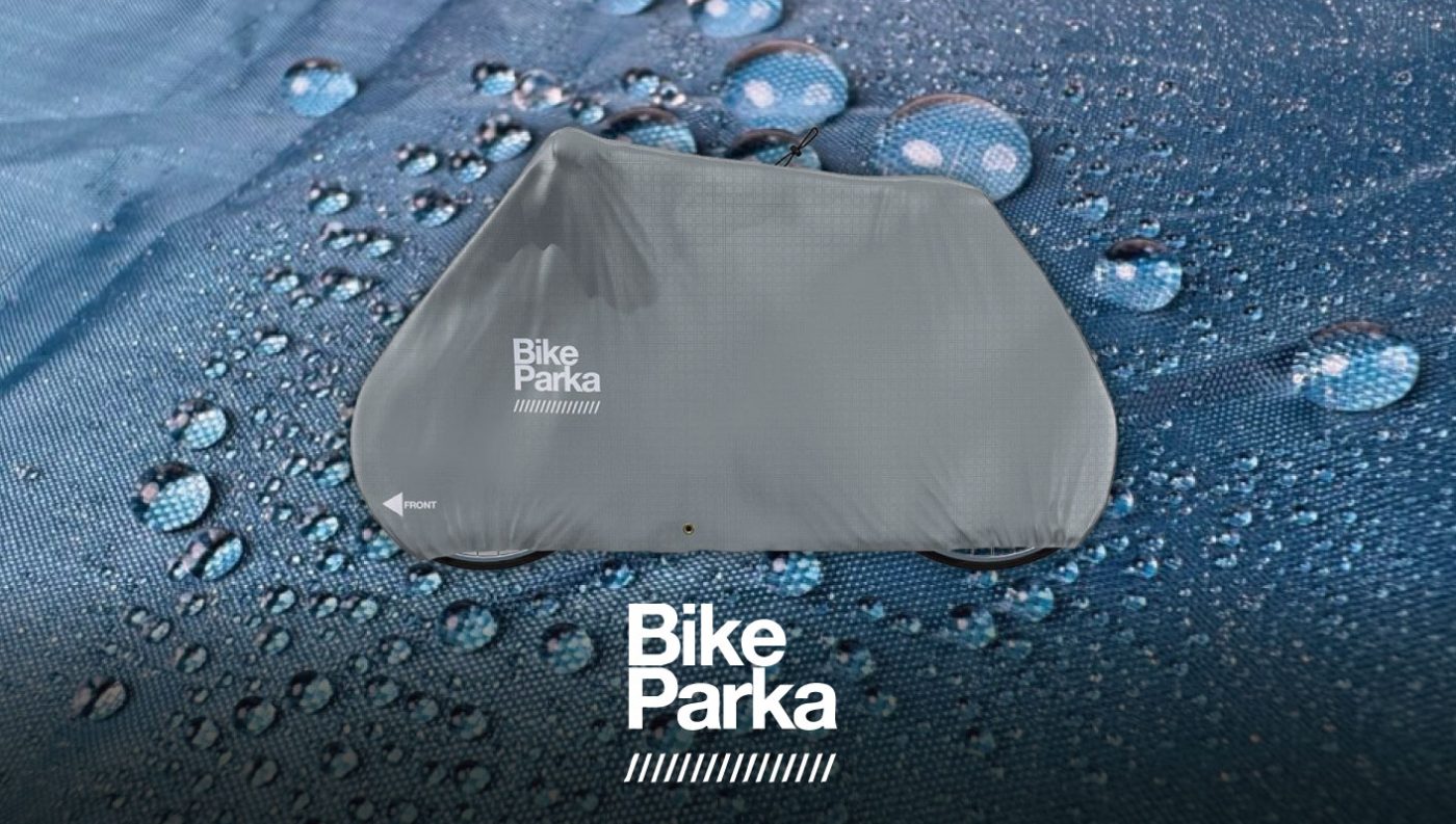Bike Parkaと書かれた灰色の自転車カバーが、水滴で覆われた青い台の上に置かれている。.