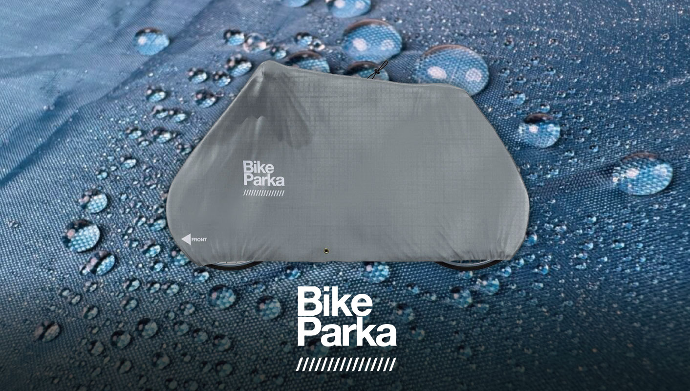 Bike Parkaと書かれた灰色の自転車カバーが、水滴で覆われた青い台の上に置かれている。.